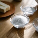 Small glass bowls of white baking powders and sugar beside sticks of butter on a wooden table