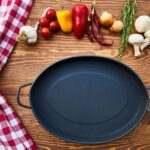 Empty black cast iron pan on a wooden table with tomatoes, peppers, garlic, rosemary and mushrooms
