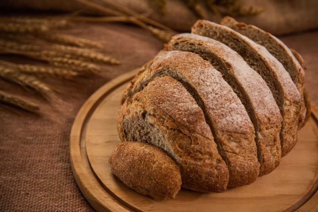 Sliced loaf of wholemeal bread on a round wooden board with ears of wheat