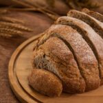 Sliced loaf of wholemeal bread on a round wooden board with ears of wheat